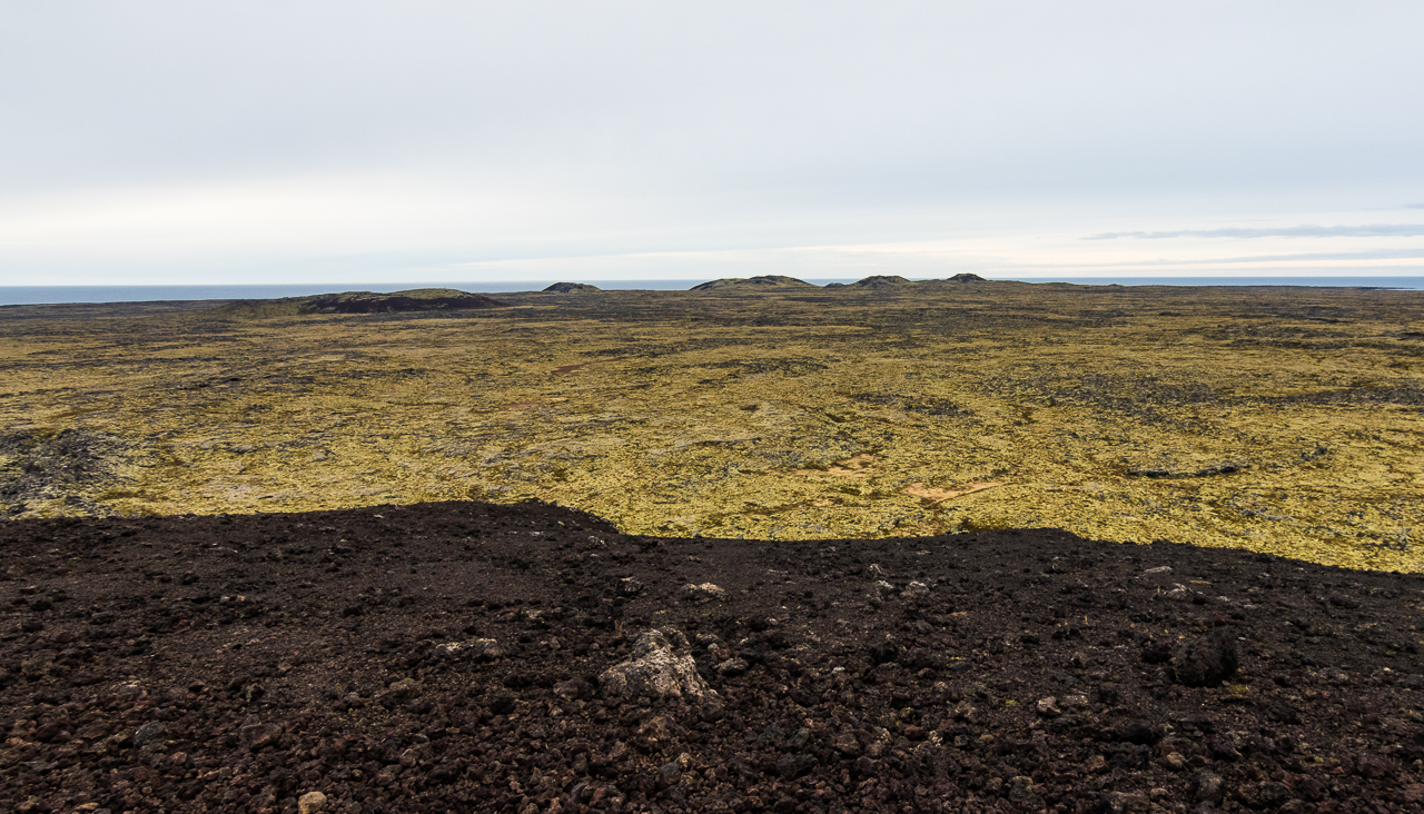 Widok ze zboczy Saxhóll w kierunku oceanu, wśród pól lawowych wystają inne wulkaniczne stożki.